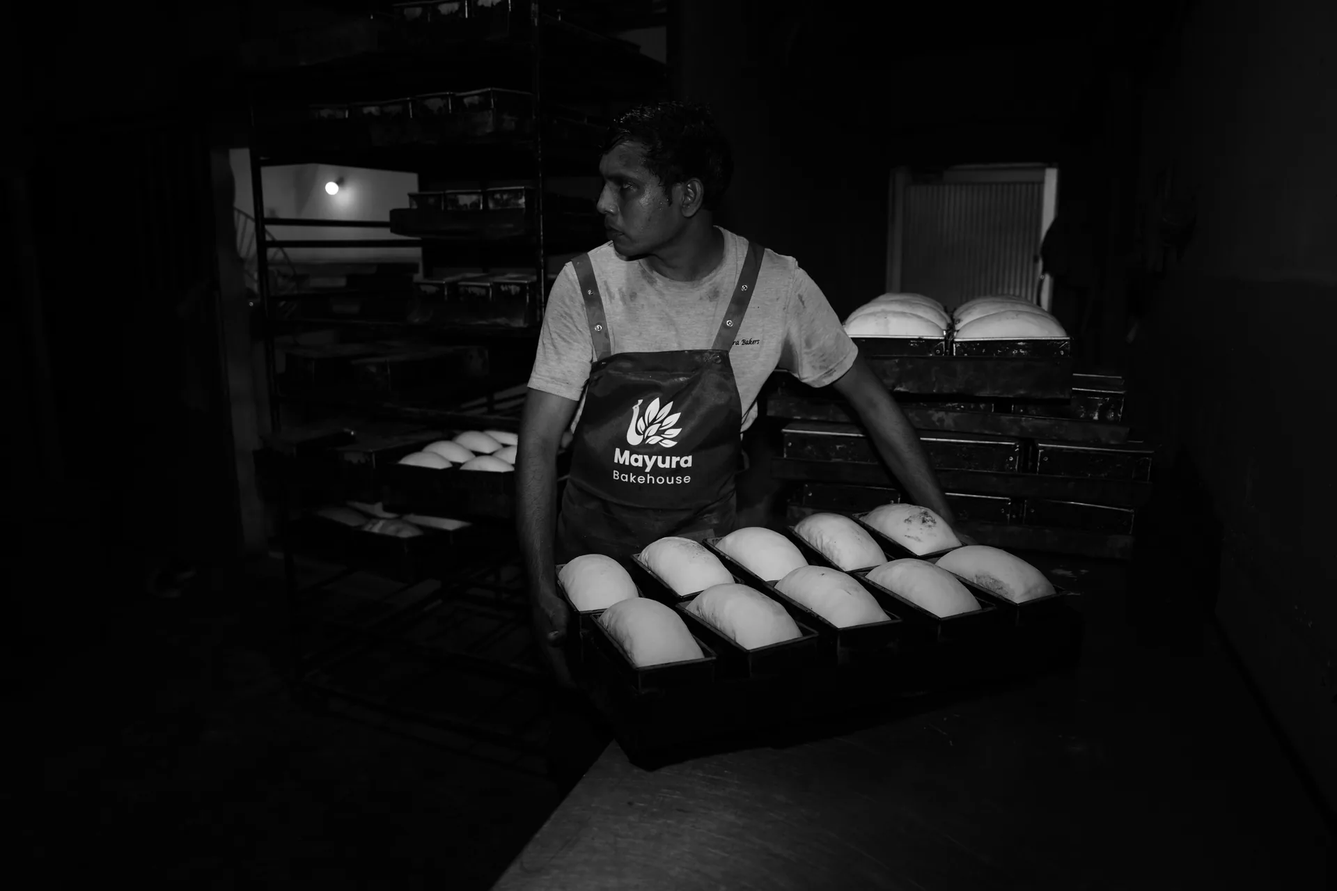 A baker carrying trays of bread dough through the bakery.