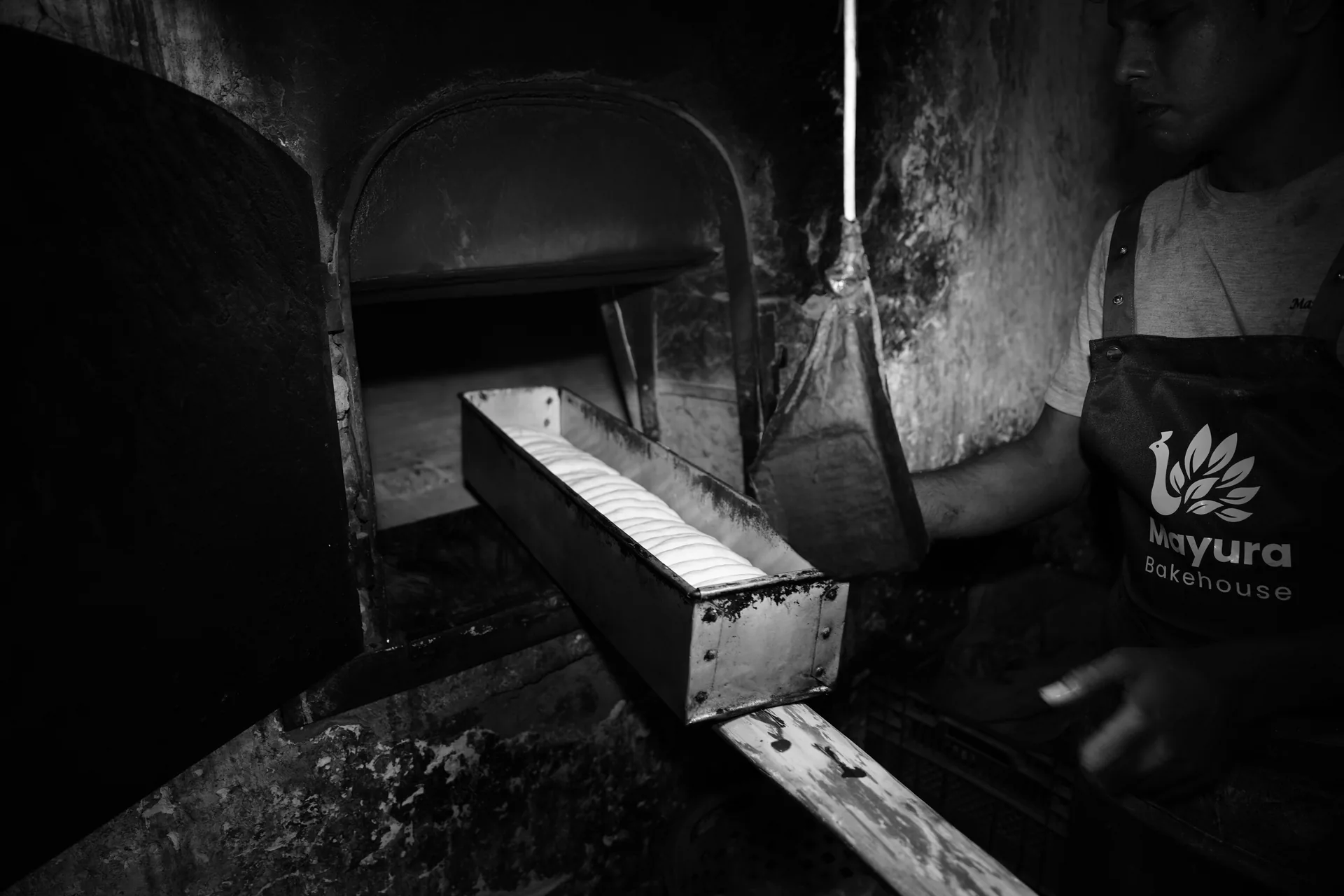 A baker dusting an oven peel with flour beside the brick oven.