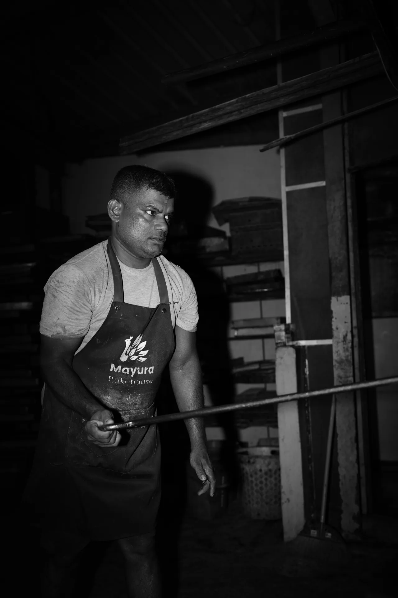 A baker holding a long oven peel beside the brick oven.