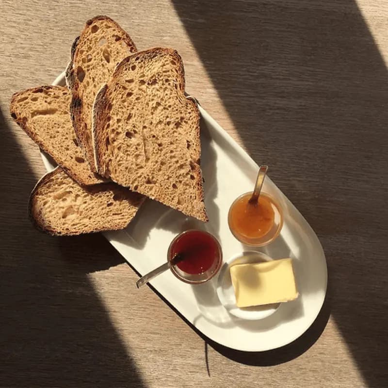 Bread, butter, and preserves laid out together in warm light.