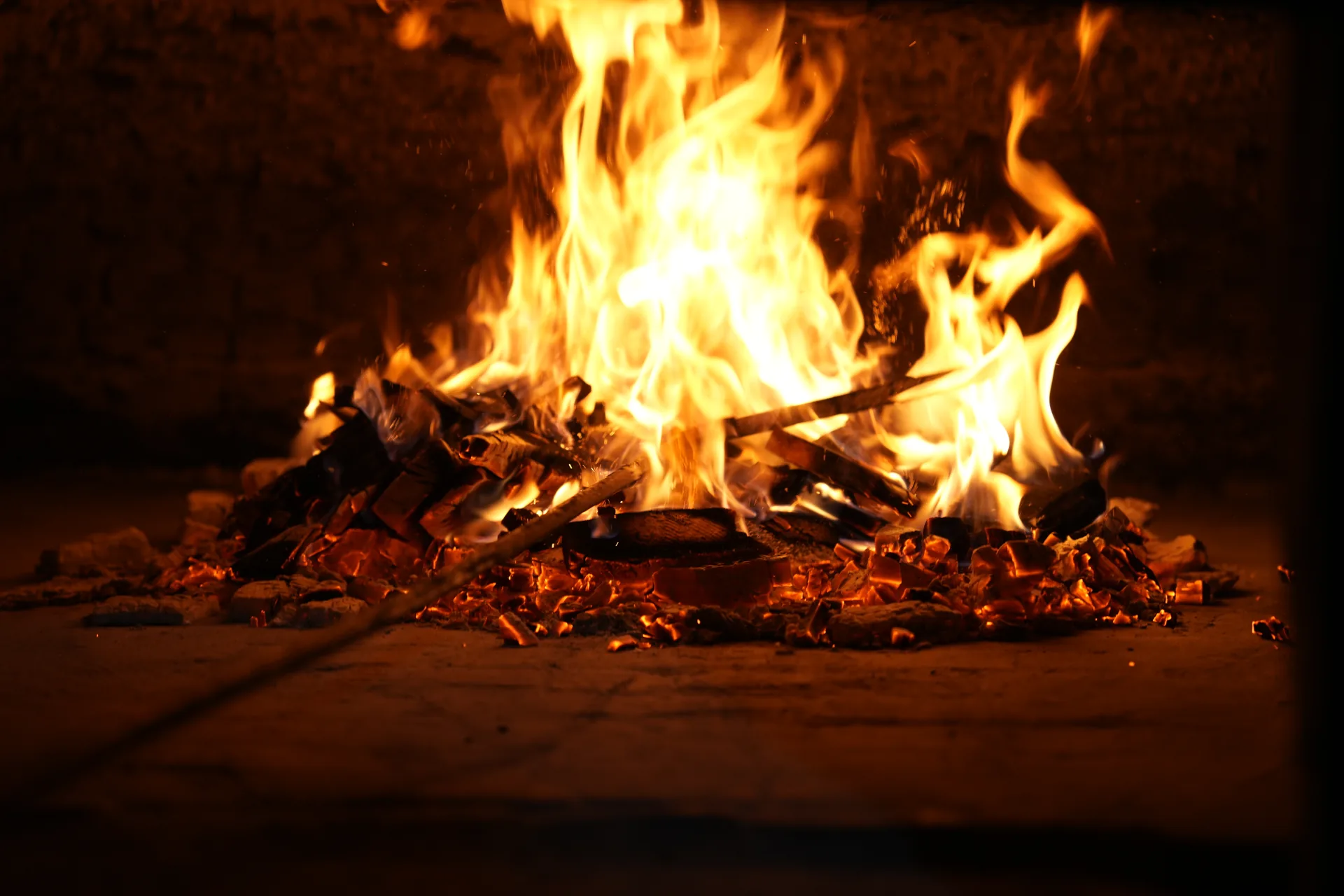 Flames rising from burning wood and glowing embers inside the bakery oven.